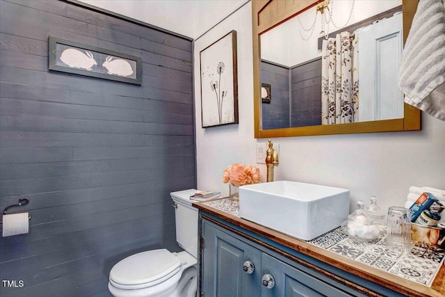 bathroom with wooden walls, toilet, and vanity