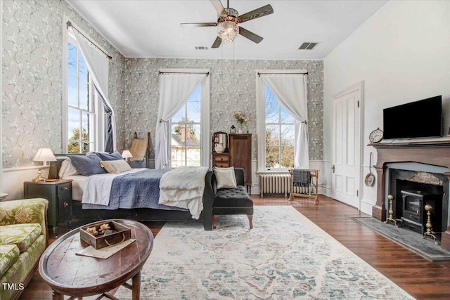 bedroom with visible vents, wood finished floors, radiator, wallpapered walls, and a wood stove