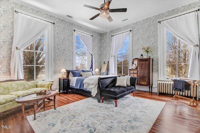 bedroom featuring visible vents, wallpapered walls, radiator heating unit, and wood finished floors