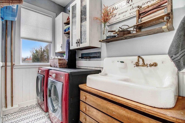 laundry area with a sink, wooden walls, cabinet space, and washer and clothes dryer