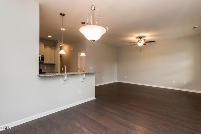 kitchen with stainless steel microwave, baseboards, decorative light fixtures, a kitchen bar, and dark wood-style floors