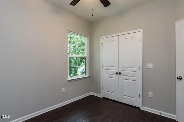 unfurnished bedroom with dark wood-style floors, a closet, baseboards, and a ceiling fan