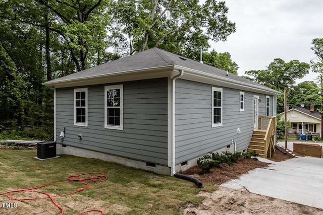 view of side of property featuring crawl space, central AC unit, a shingled roof, and a yard