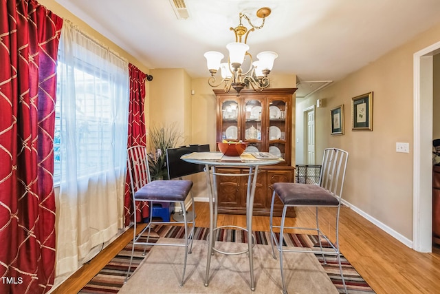 dining space with visible vents, baseboards, attic access, wood finished floors, and a notable chandelier