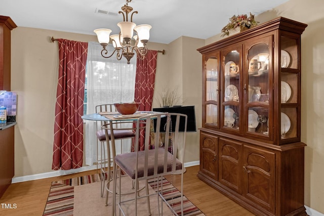 dining room featuring visible vents, baseboards, light wood-style floors, and a notable chandelier