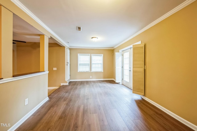 empty room with wood finished floors, baseboards, and ornamental molding