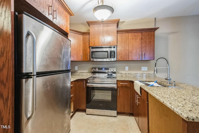 kitchen featuring a sink, stainless steel appliances, light stone counters, and brown cabinetry