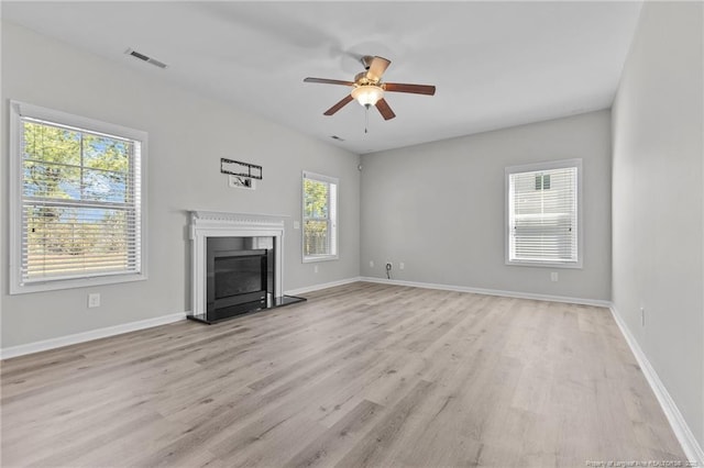 unfurnished living room with a glass covered fireplace, baseboards, visible vents, and light wood-type flooring