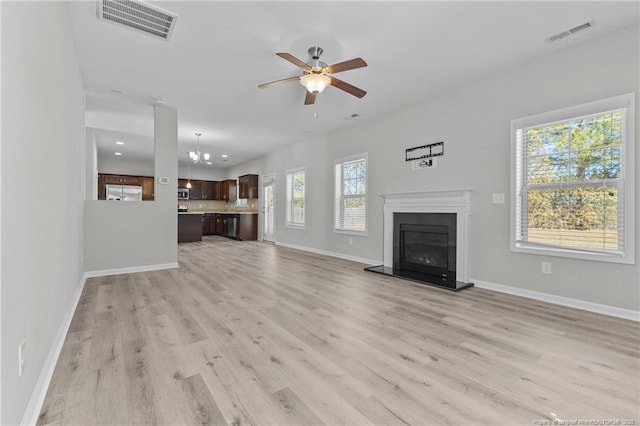 unfurnished living room featuring visible vents, baseboards, light wood-style floors, and a glass covered fireplace