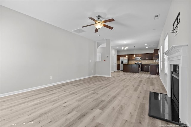 unfurnished living room featuring visible vents, light wood-style flooring, a sink, baseboards, and ceiling fan