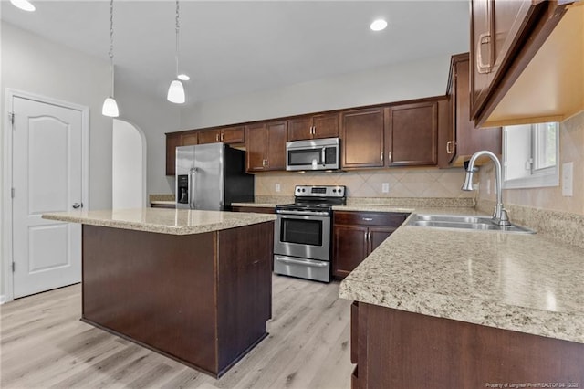 kitchen featuring tasteful backsplash, light wood-style flooring, arched walkways, stainless steel appliances, and a sink