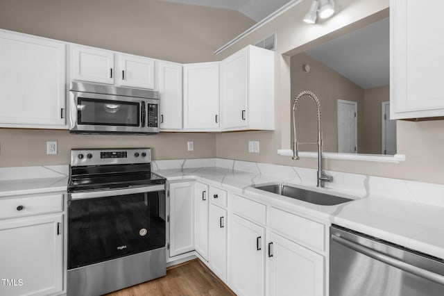 kitchen featuring visible vents, a sink, appliances with stainless steel finishes, white cabinets, and vaulted ceiling