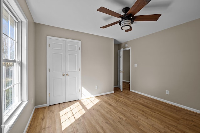 unfurnished bedroom with light wood finished floors, a closet, baseboards, and a ceiling fan