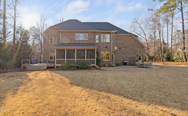 rear view of property with brick siding, a sunroom, a deck, a yard, and a patio