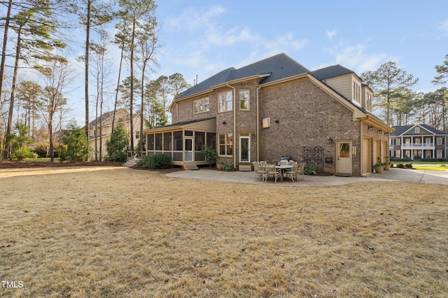 rear view of property featuring brick siding, a yard, a sunroom, a patio area, and driveway