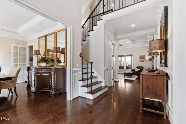 entrance foyer with crown molding, a wainscoted wall, stairs, a decorative wall, and dark wood-style flooring