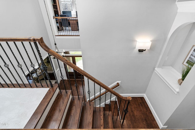 stairway with baseboards, arched walkways, wood finished floors, and a towering ceiling