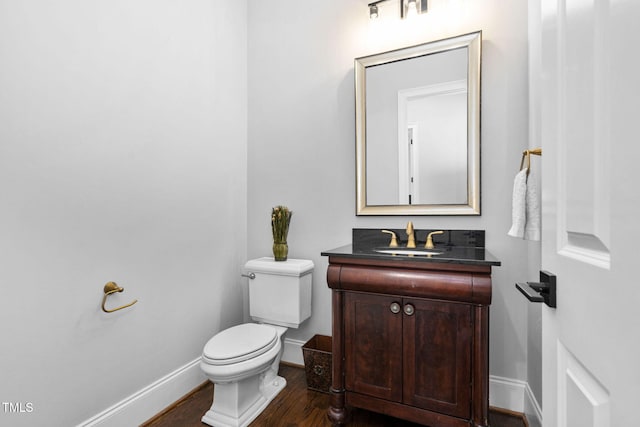 half bathroom featuring baseboards, toilet, wood finished floors, and vanity