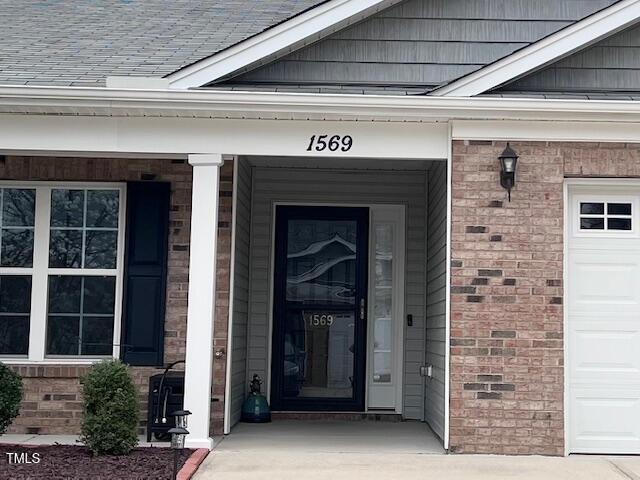 entrance to property with brick siding, a shingled roof, and a garage