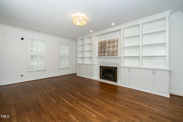 unfurnished living room with built in shelves, baseboards, a fireplace, ornamental molding, and dark wood-type flooring