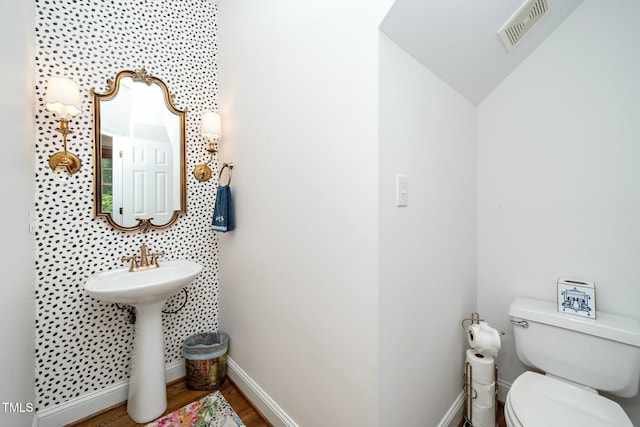 half bathroom featuring wood finished floors, visible vents, baseboards, a sink, and toilet