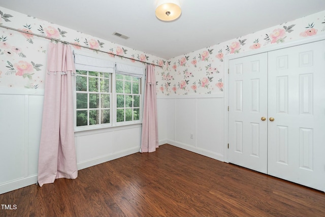 unfurnished bedroom with visible vents, wallpapered walls, wainscoting, wood finished floors, and a closet