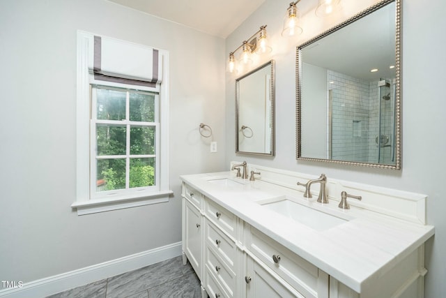 full bath featuring a sink, tiled shower, baseboards, and double vanity