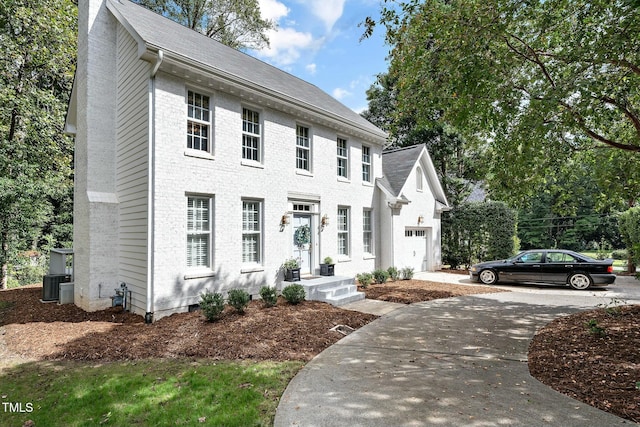 colonial home featuring driveway, a shingled roof, brick siding, central AC unit, and a chimney