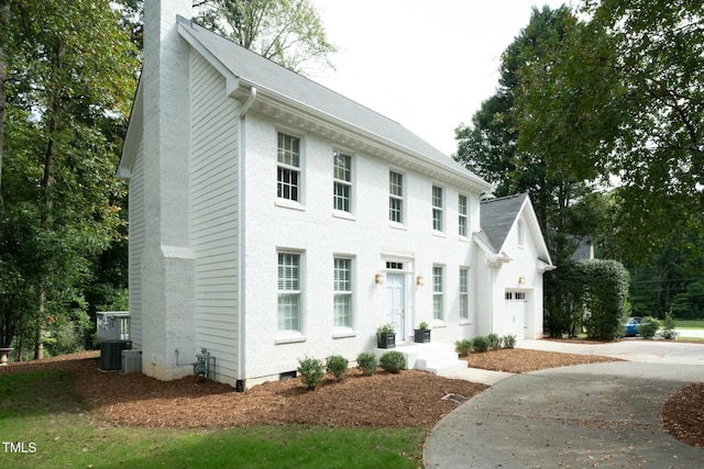 colonial house featuring driveway, an attached garage, central AC, a chimney, and brick siding