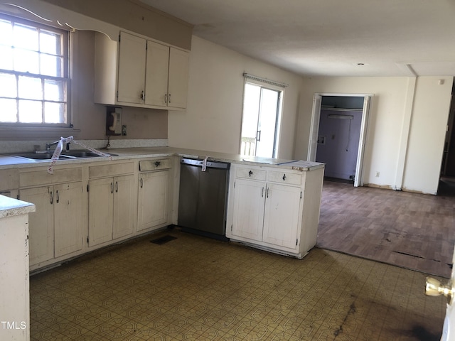 kitchen featuring a sink, stainless steel dishwasher, a peninsula, dark floors, and light countertops