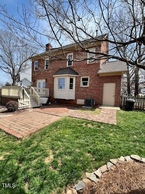 back of property featuring brick siding, a patio area, a lawn, and a chimney