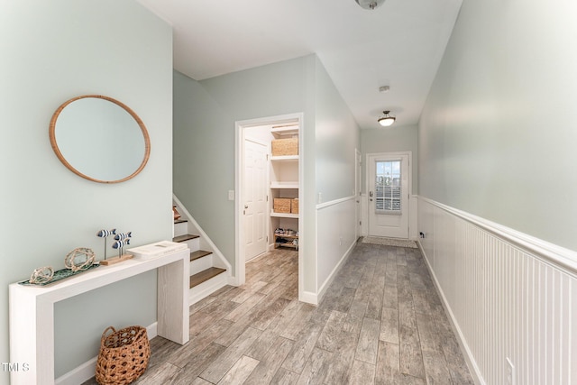 hallway featuring stairs, wainscoting, and light wood finished floors