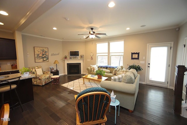 living room with a fireplace, dark wood finished floors, a ceiling fan, and crown molding