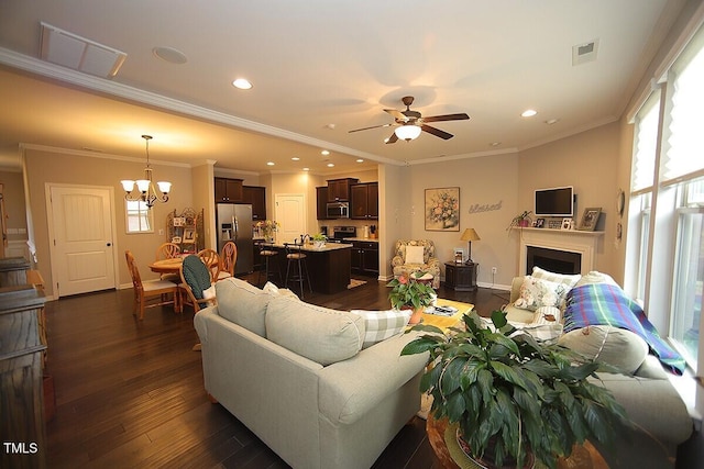 living room with visible vents, ceiling fan with notable chandelier, a fireplace, baseboards, and dark wood-style flooring