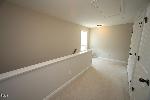 hallway featuring light carpet, attic access, and baseboards