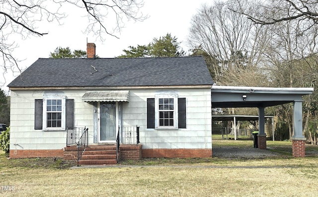 view of front facade with a chimney, an attached carport, a shingled roof, and a front lawn