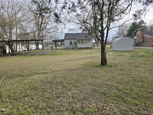 view of yard with a storage shed, an attached carport, an outbuilding, and fence