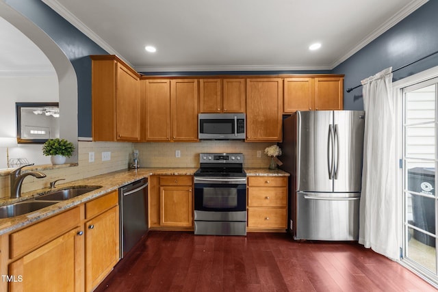 kitchen featuring dark wood-type flooring, light stone countertops, appliances with stainless steel finishes, arched walkways, and a sink