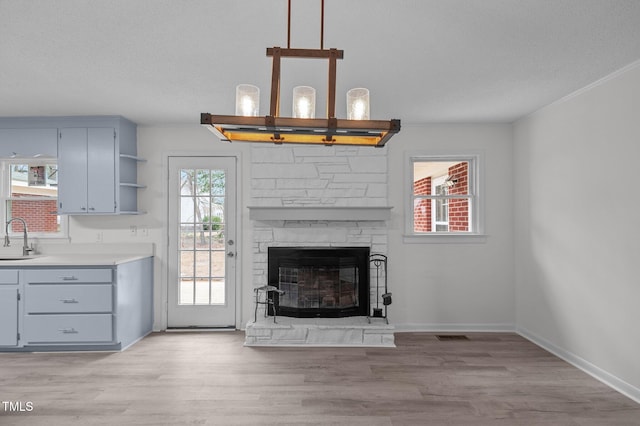 205 Woodside Dr, Goldsboro, NC 27534 - unfurnished living room featuring a sink, a textured ceiling, a stone fireplace, light wood finished floors, and baseboards