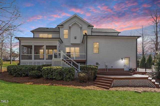 back of house at dusk featuring a lawn, fence, stairway, a sunroom, and a wooden deck