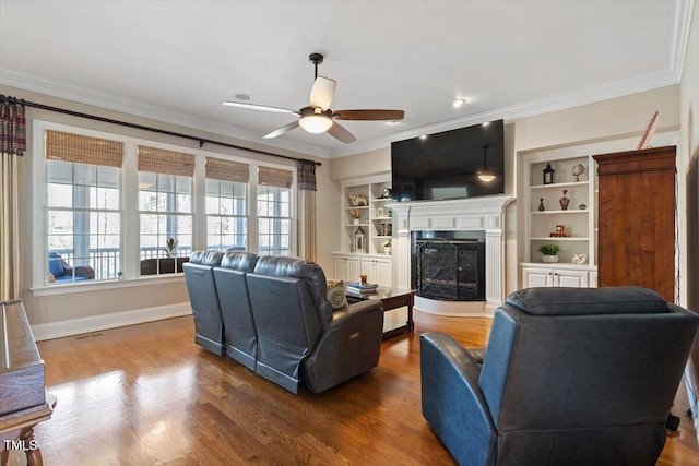 living area featuring a fireplace with raised hearth, crown molding, baseboards, and wood finished floors