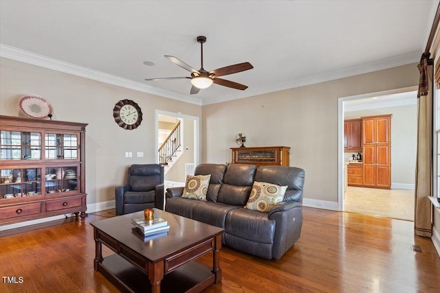 living area featuring stairway, wood finished floors, baseboards, ceiling fan, and ornamental molding