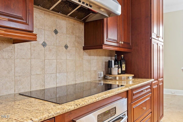 kitchen with oven, black electric stovetop, under cabinet range hood, light stone counters, and decorative backsplash