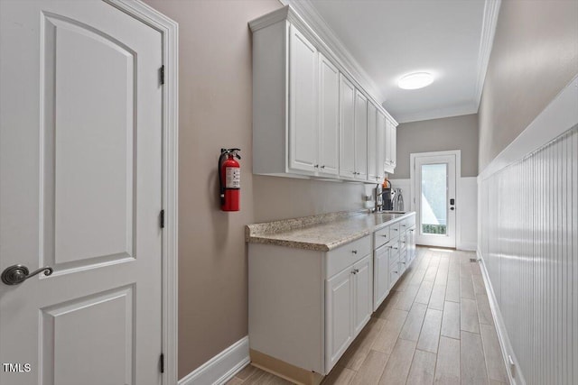 kitchen featuring crown molding, light countertops, light wood-style floors, white cabinetry, and a sink