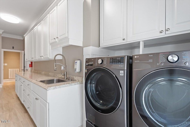 clothes washing area featuring light wood finished floors, cabinet space, separate washer and dryer, ornamental molding, and a sink