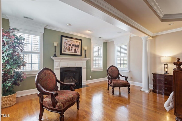 living area with crown molding, baseboards, a fireplace with flush hearth, decorative columns, and wood finished floors