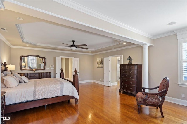 bedroom featuring a raised ceiling, decorative columns, wood finished floors, and baseboards