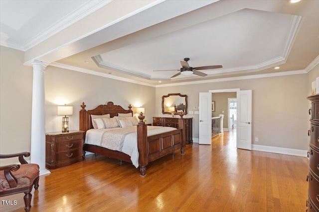 bedroom with a tray ceiling, crown molding, wood finished floors, and ornate columns