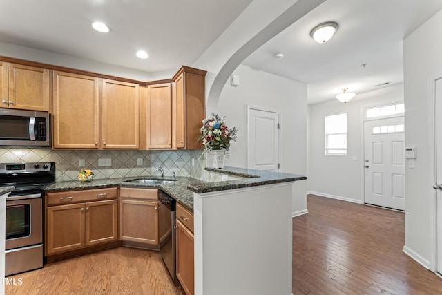 kitchen with a sink, stainless steel appliances, a peninsula, and light wood-style flooring