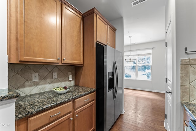 kitchen with tasteful backsplash, dark stone counters, brown cabinets, stainless steel refrigerator with ice dispenser, and hardwood / wood-style flooring